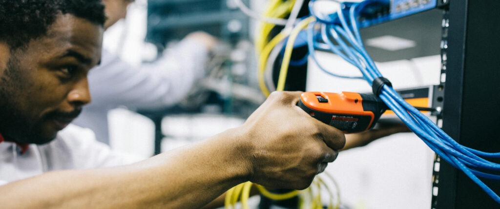 A technology worker holds a testing device next to wiring.
